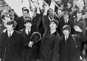 A black and white photo of the Beatles waving to a crowd